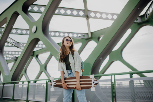 Young woman walking on city bridge with a skateboard. Youth culture and commuting concept.