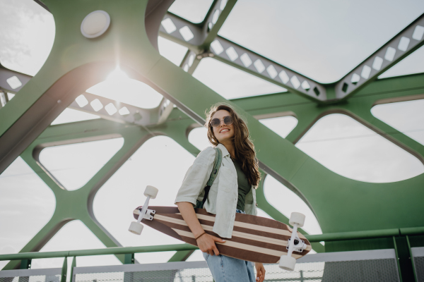 Young woman walking on city bridge with a skateboard. Youth culture and commuting concept.