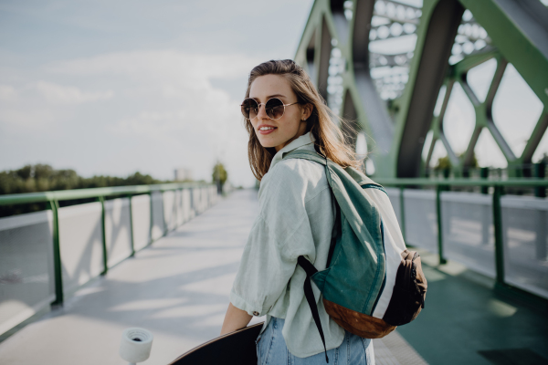 Young woman walking on city bridge with a skateboard. Youth culture and commuting concept.