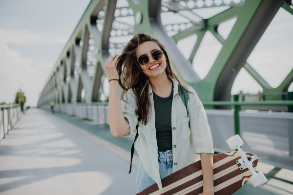 Young woman walking on city bridge with a skateboard. Youth culture and commuting concept.