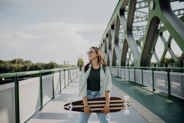 Young woman walking on city bridge with a skateboard. Youth culture and commuting concept.