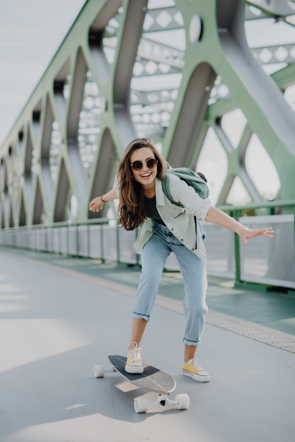 Young woman ridding a skateboard at city bridge. Youth culture and commuting concept.