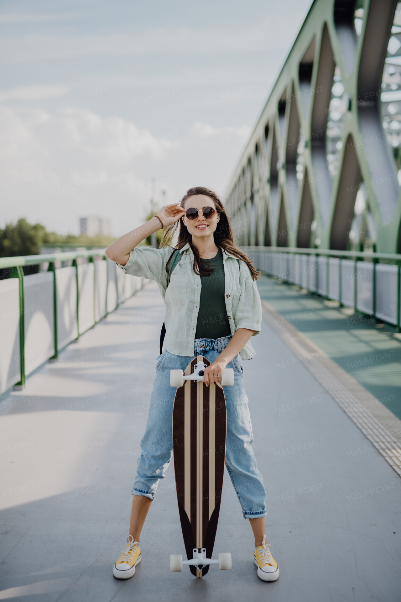 Young woman walking on city bridge with a skateboard. Youth culture and commuting concept.