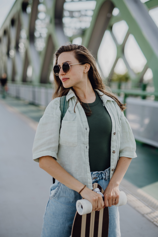 Young woman posing on city bridge with a skateboard. Youth culture and commuting concept.