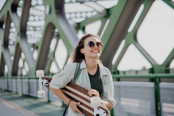 Young woman walking on city bridge with a skateboard. Youth culture and commuting concept.