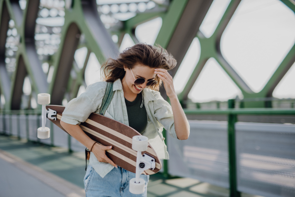 Young woman walking on city bridge with a skateboard. Youth culture and commuting concept.