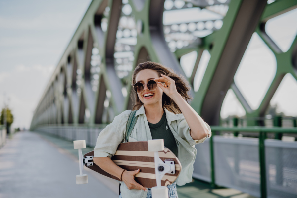 Young woman walking on city bridge with a skateboard. Youth culture and commuting concept.