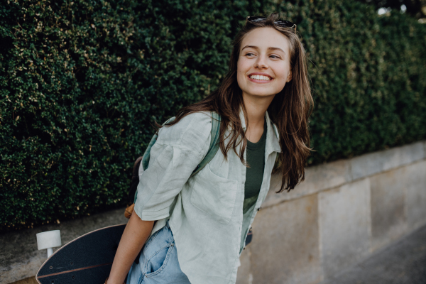 Portrait of young happy woman outdoor with a skateboard. Youth culture and commuting concept.