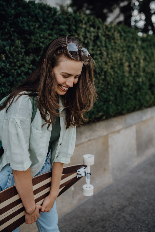 Portrait of young happy woman outdoor with a skateboard. Youth culture and commuting concept.