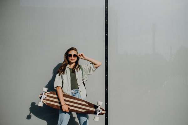 Portrait of young woman outdoor with a skateboard. Youth culture and commuting concept.