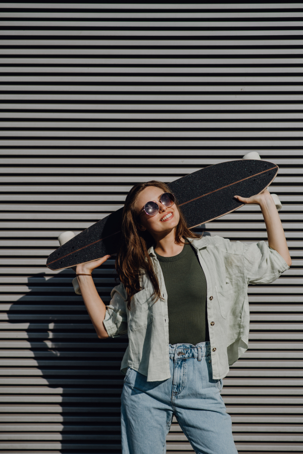 Portrait of young happy woman outdoor with a skateboard. Youth culture and commuting concept.