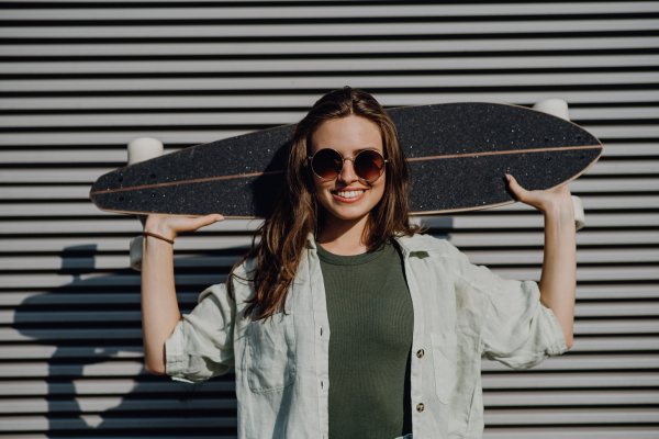 Portrait of young happy woman outdoor with a skateboard. Youth culture and commuting concept.