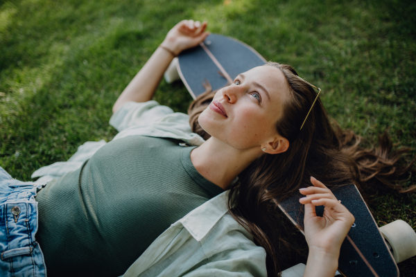 High angle view of young woman lying on the grass with a skateboard.