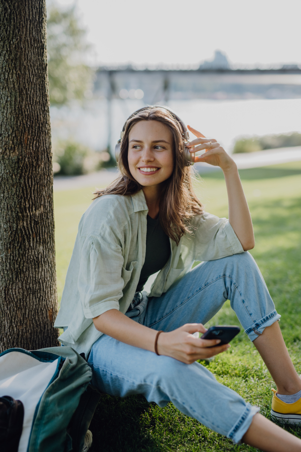 Portrait of young woman listening the music trough headphones in city park.