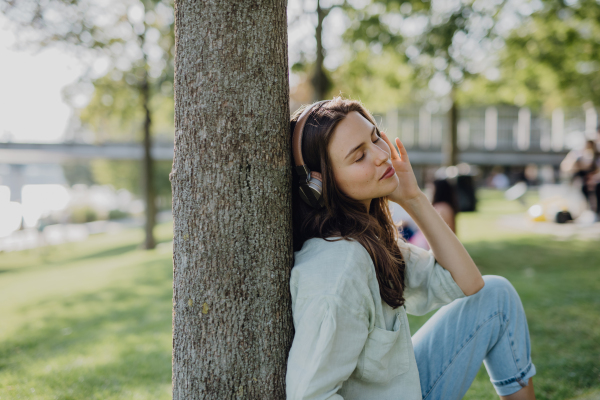 Portrait of young woman listening the music trough headphones in city park.