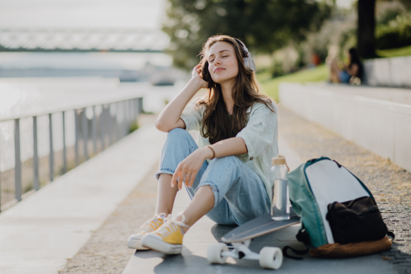 Happy young woman sitting in a city and listening music. Youth culture and commuting concept.