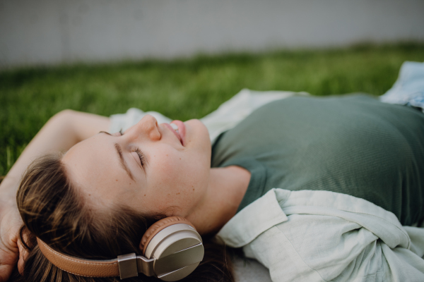 Portrait of young woman lying on a lawn listening the music trough headphones.