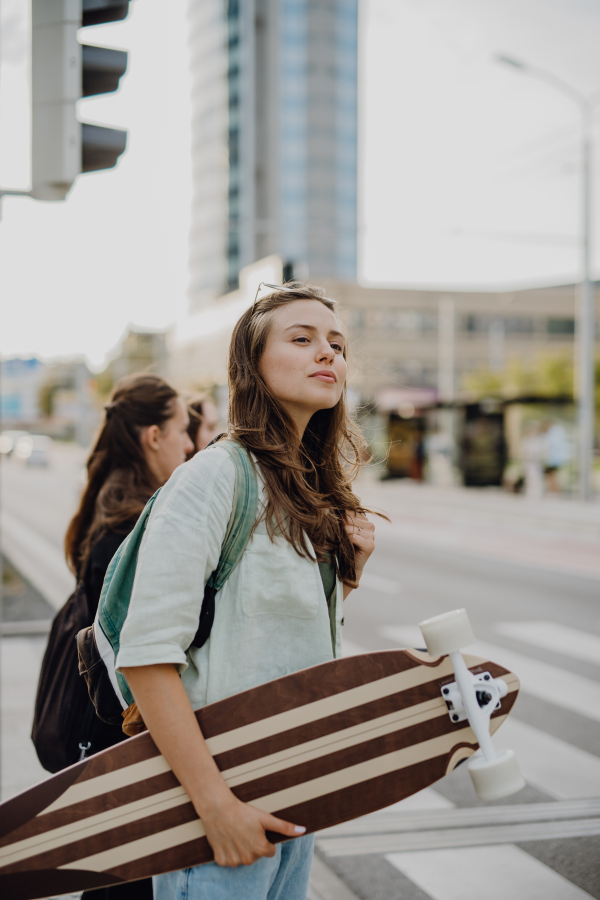 Young woman walking in city with a skateboard. Youth culture and commuting concept.