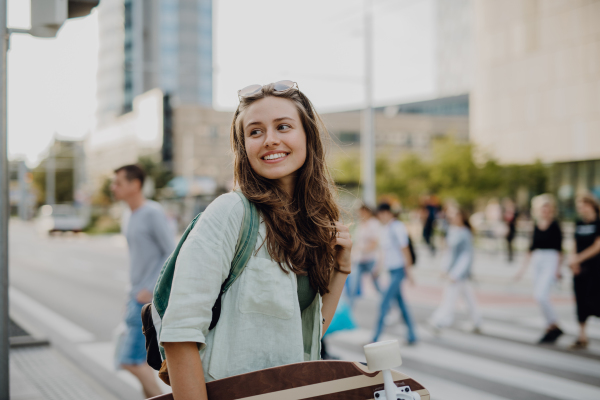 Young woman walking in city with a skateboard. Youth culture and commuting concept.