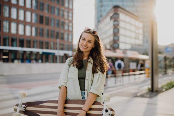 Young woman walking in city with a skateboard. Youth culture and commuting concept.