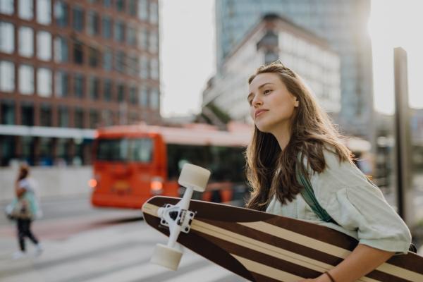 Young woman walking in city with a skateboard. Youth culture and commuting concept.