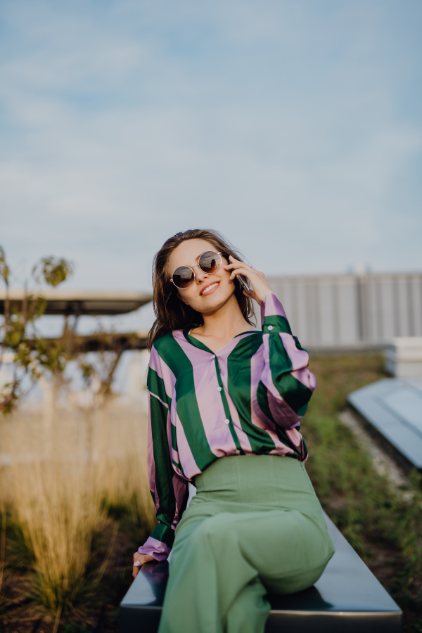 Portrait of beautiful young woman with smartphone outdoor in a city, during sunset.