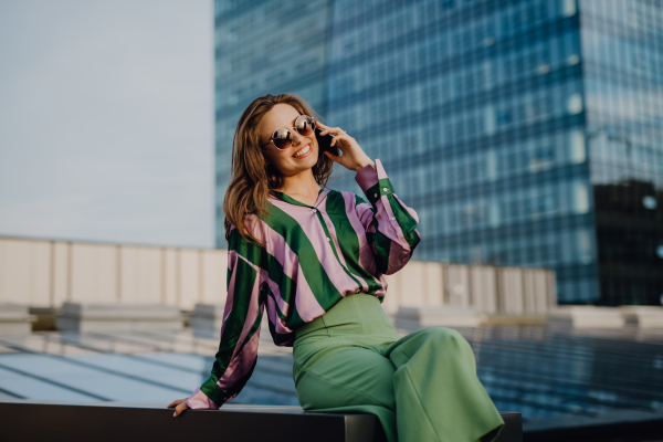 Portrait of beautiful young woman with smartphone outdoor in a city, during sunset.