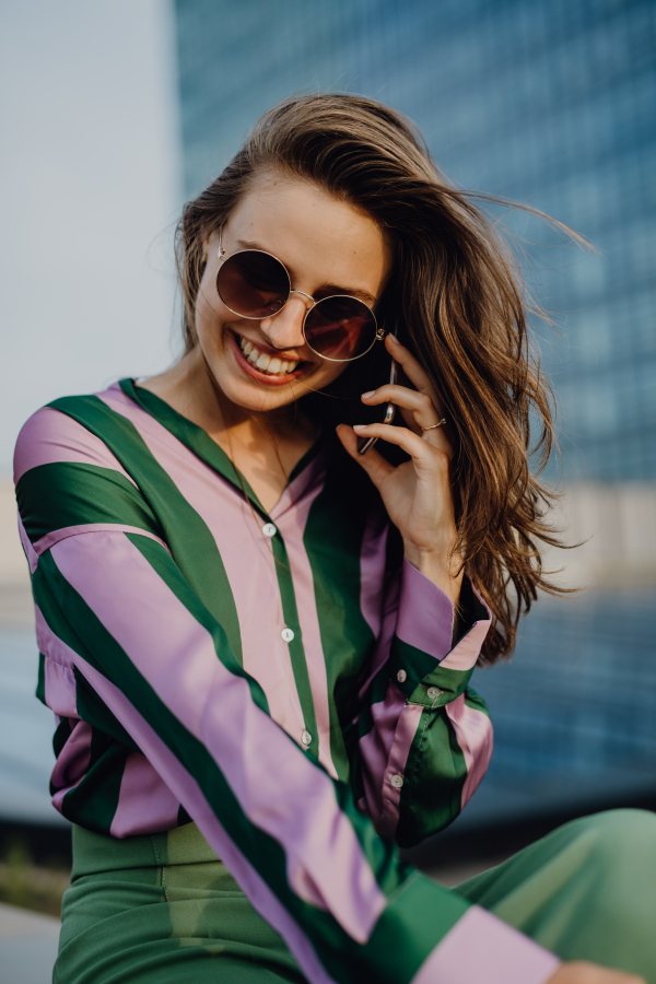 Portrait of beautiful young woman with smartphone outdoor in a city, during sunset.