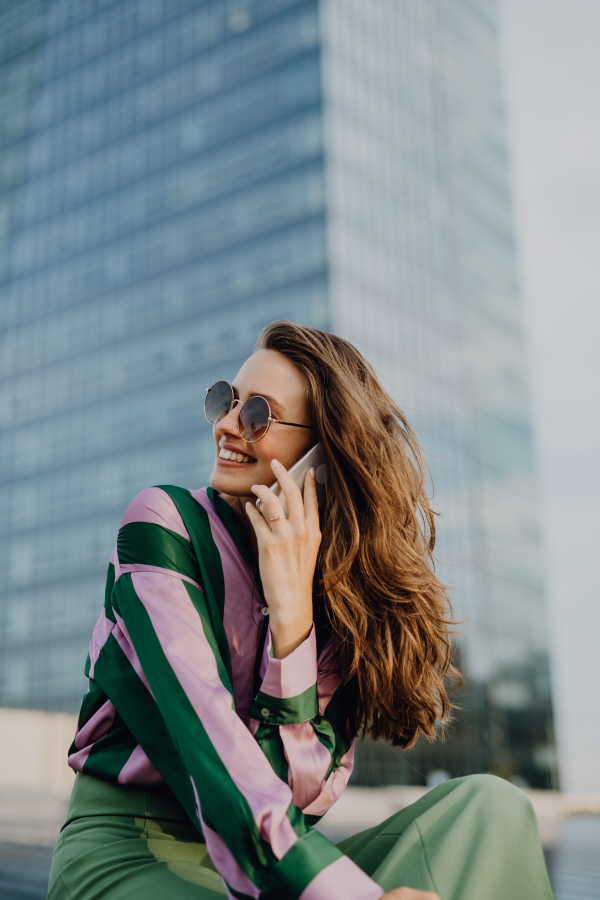 Portrait of beautiful young woman with smartphone outdoor in a city, during sunset.