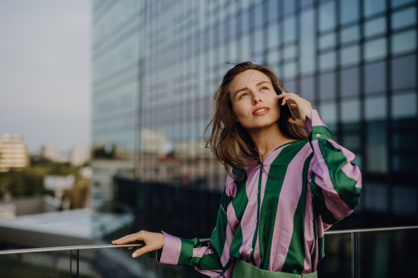 Portrait of beautiful young woman with smartphone outdoor in a city, during sunset.