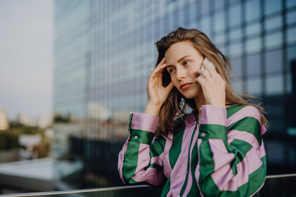 Portrait of beautiful young woman with smartphone outdoor in a city, during sunset.