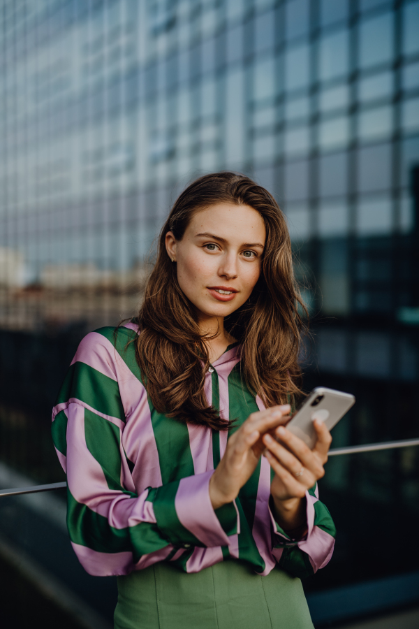 Portrait of beautiful young woman with smartphone outdoor in a city, during sunset.