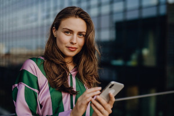 Portrait of beautiful young woman with smartphone outdoor in a city, during sunset.