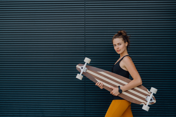 Portrait of young woman outdoor with a skateboard. Youth culture and commuting concept.