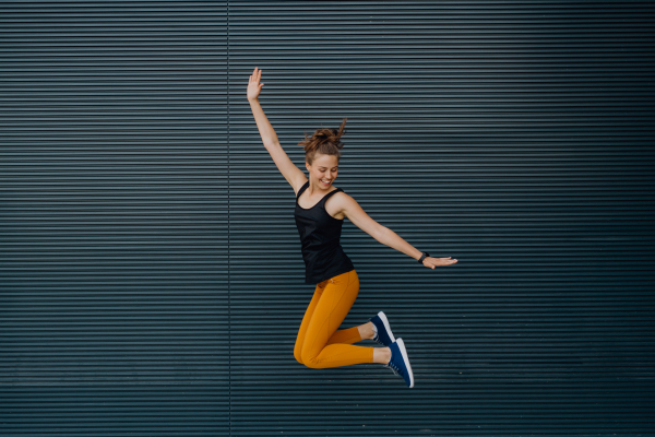 Portrait of young excited woman jumping outdoor in a city.