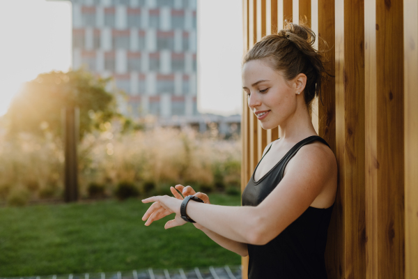 Young woman checking a smartwatch in city, preparing for run, healthy lifestyle and sport concept.