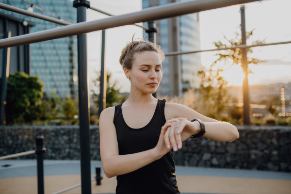 Young woman checking a smartwatch in city, preparing for run, healthy lifestyle and sport concept.