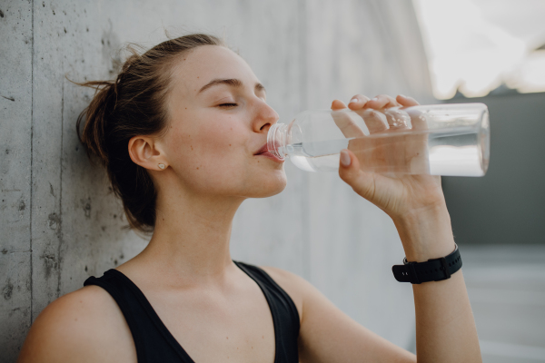 Young woman drinking water during jogging in a city, healthy lifestyle and sport concept.