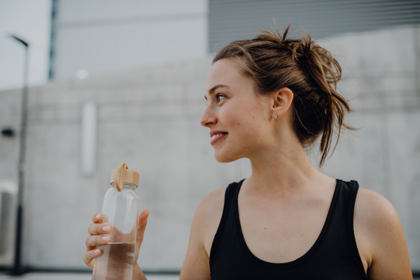 Young woman drinking water during jogging in a city, healthy lifestyle and sport concept.