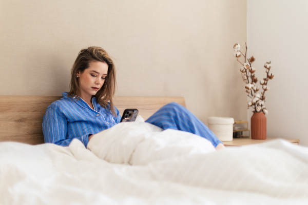 Young woman lying on her bed and scrolling a smartphone.