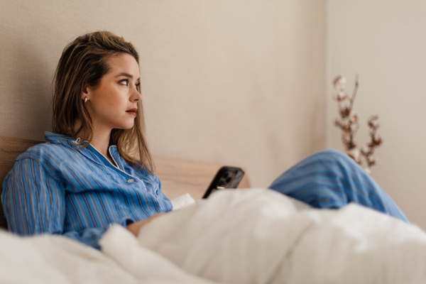 Young woman lying on her bed and scrolling a smartphone.