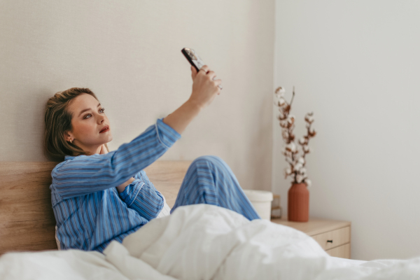 Young happy woman taking selfie in a bed.