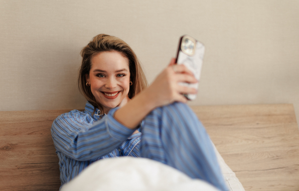 Young woman lying on her bed and scrolling a smartphone.