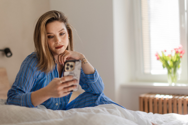 Young woman lying on her bed and scrolling a smartphone.