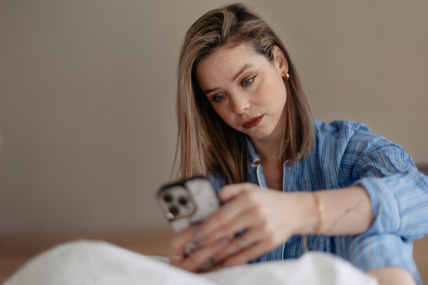 Young woman lying on her bed and scrolling a smartphone.