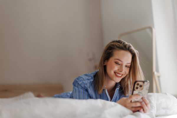 Young woman lying on her bed and scrolling a smartphone.