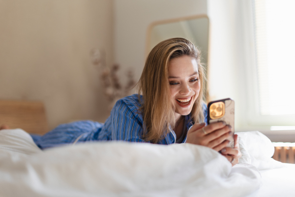 Young woman lying on her bed and scrolling a smartphone.