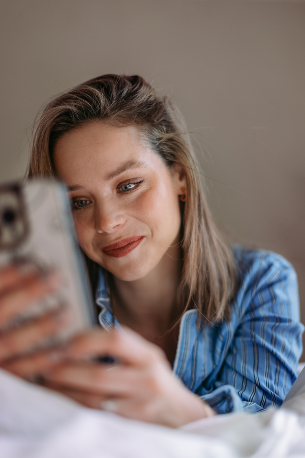 Young woman lying on her bed and scrolling a smartphone.