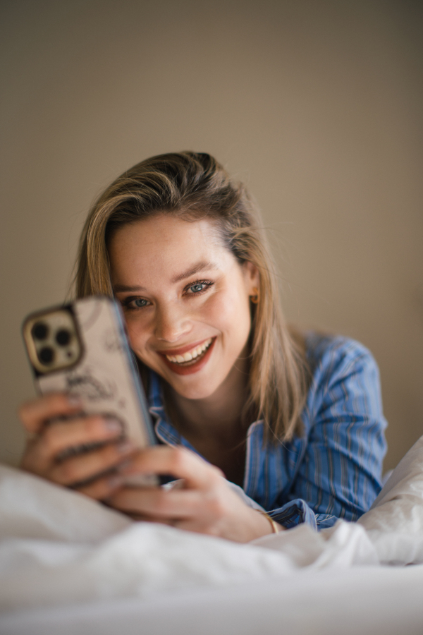 Young woman lying on her bed and scrolling a smartphone.