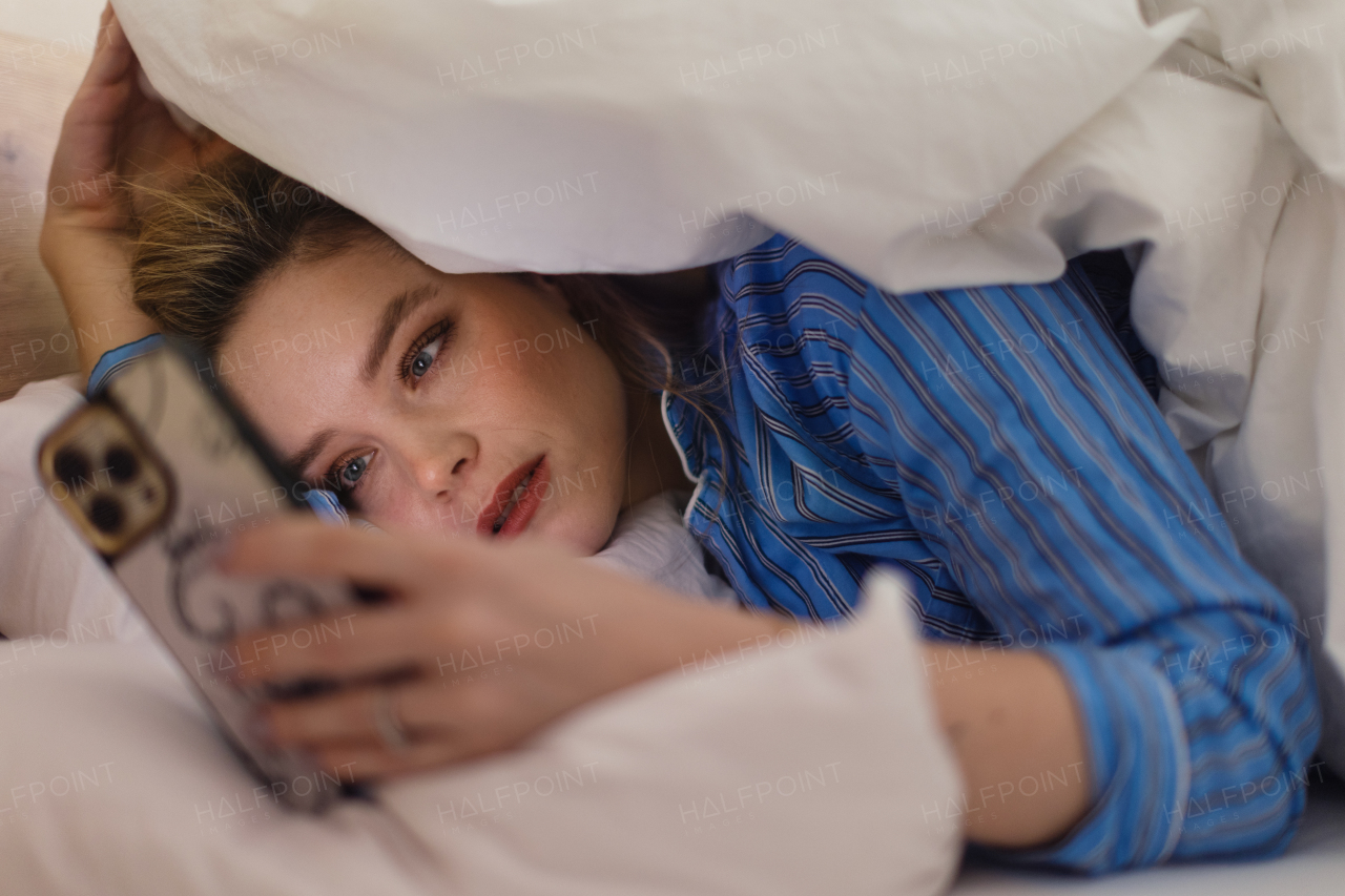 Young woman lying on her bed and scrolling a smartphone.